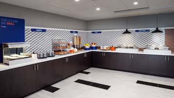 Un área de cocina moderna con secciones identificadas para panadería, cereales, fruta y alimentos calientes.