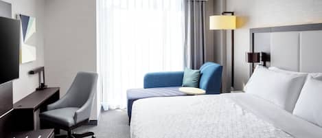 A hotel room with a bed, a desk, a chair, a TV, and a window with curtains.