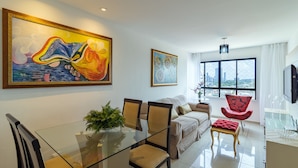A modern living room with a glass dining table, beige sofa, red armchair, and large paintings on the walls. - Excelente comodidade em Recife (Recife)