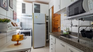 A modern kitchen with white cabinets, a stainless steel refrigerator, a microwave, and a granite countertop. - Excelente comodidade em Recife (Recife)