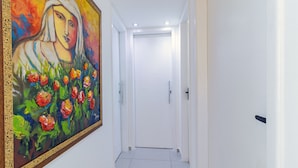 A hallway with a large painting on the left wall, a white door at the end, and a tiled floor. - Excelente comodidade em Recife (Recife)
