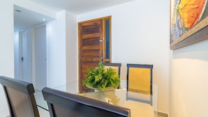 A dining area with a glass table, wooden chairs, a potted plant, and a wooden door. - Excelente comodidade em Recife (Recife)