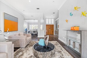 Uma sala de estar moderna com um grande quadro abstrato, uma mesa de centro de vidro e uma lareira com objetos decorativos.