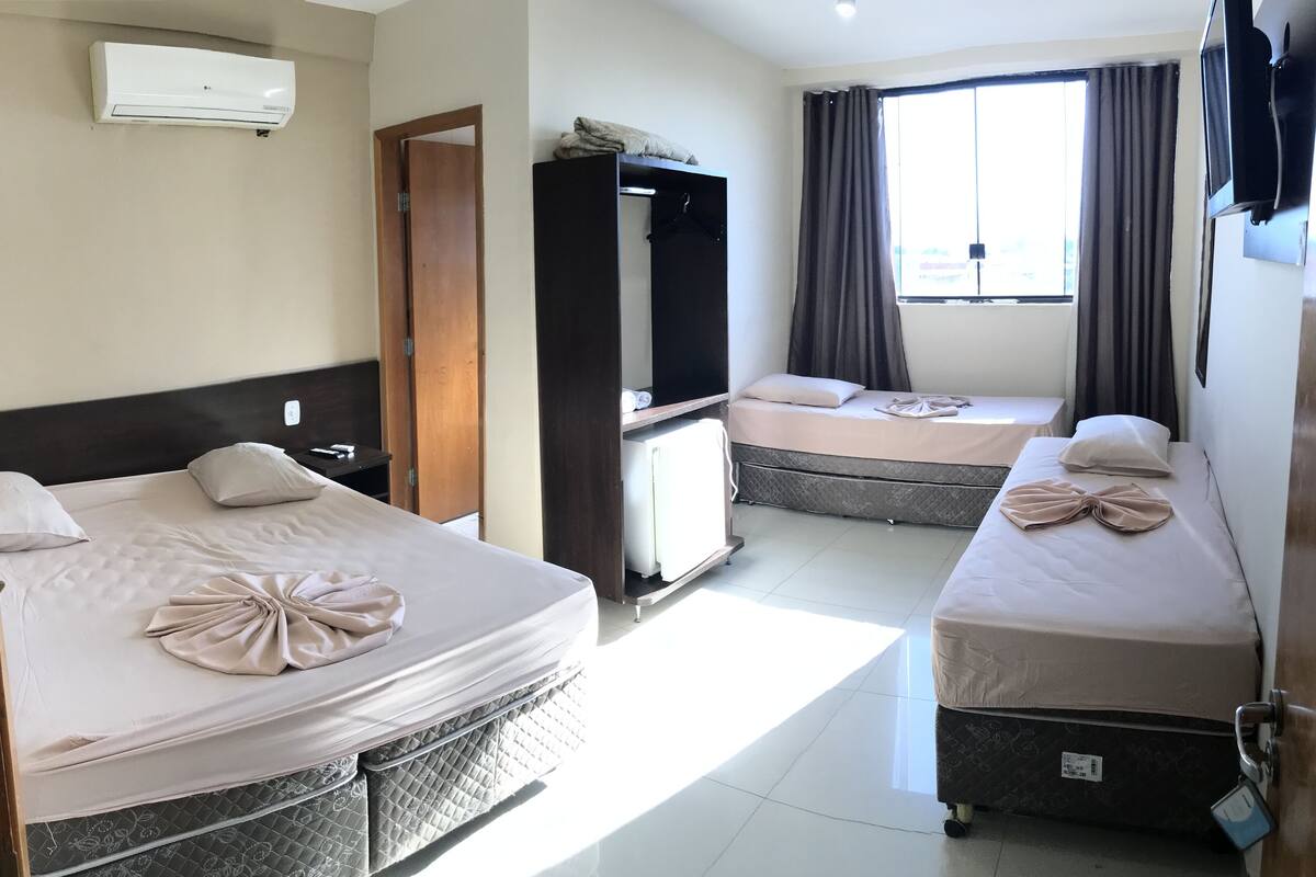 Habitación de hotel con dos camas, un armario, un televisor y una ventana con cortinas.