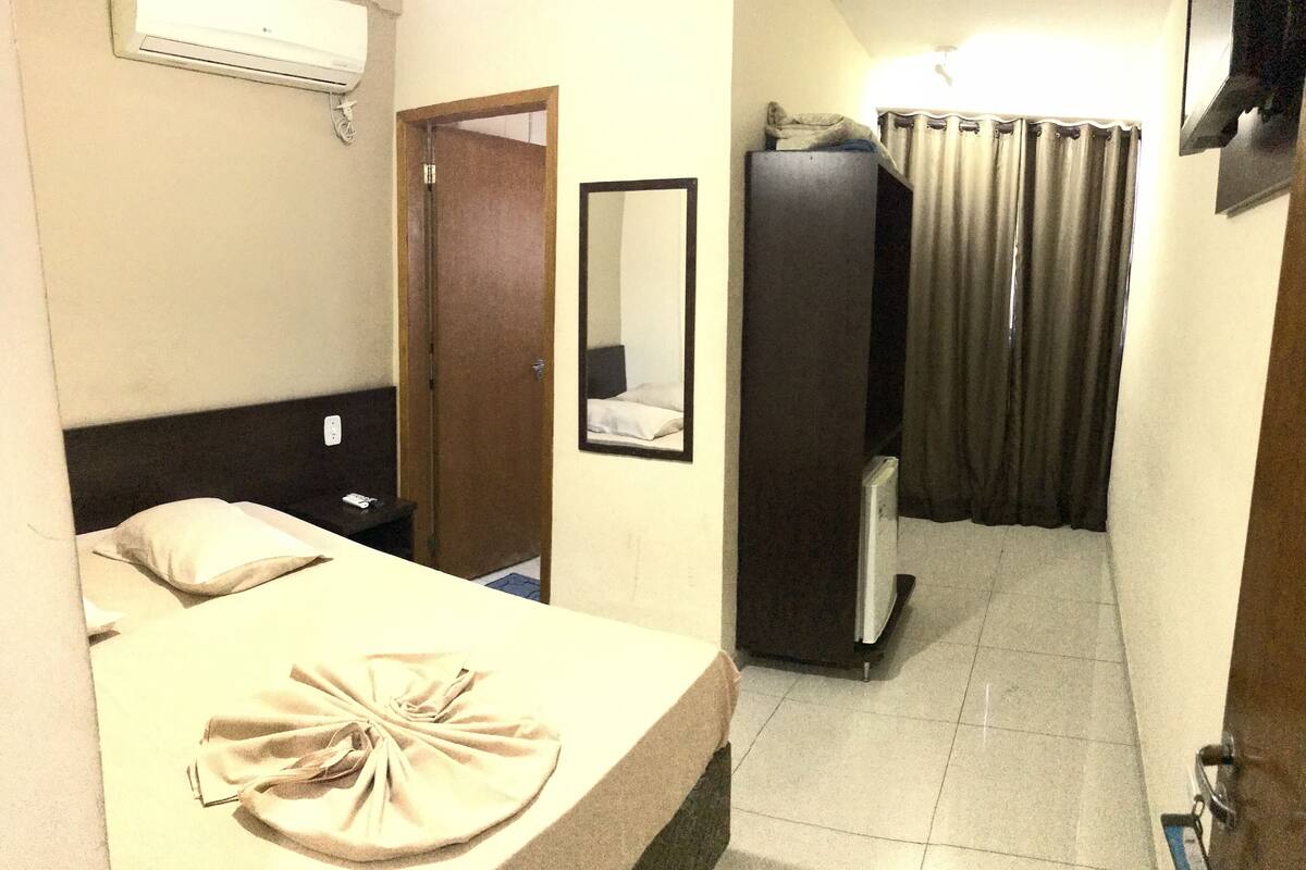 Una habitación de hotel con una cama, un espejo, un armario y una cortina.