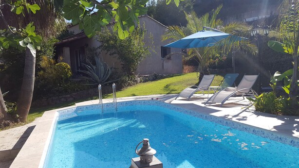 Ein Swimmingpool mit einer Fontäne, umgeben von Liegestühlen und einem blauen Sonnenschirm.