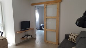 Ein Wohnzimmer mit Fernseher auf einer Holzregal, einer Couch und einer Schiebetür zu einem weiteren Raum.
