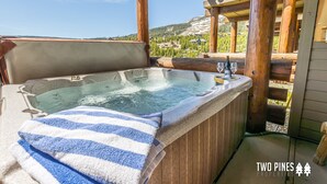 Un bain à remous avec une serviette à rayures, une terrasse en bois et une vue sur une montagne et une forêt.