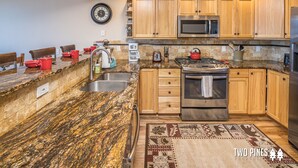 Une cuisine dotée de plans de travail en granit, de meubles en bois, d’appareils électroménagers en acier inoxydable et d’un tapis à motifs.