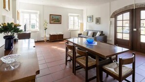 A spacious living room with a wooden dining table, comfortable seating, a sofa, and a large window providing natural light. - Renovated Grange in a Renaissance Villa Park (Capannori)
