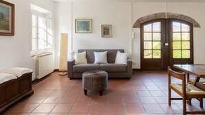 A living room with a sofa, ottoman, and wooden furniture. There are windows and a door with an arch. - Renovated Grange in a Renaissance Villa Park (Capannori)