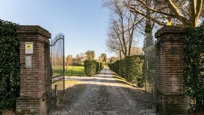 A gated entrance to a property with a paved driveway leading to a hedge-lined path. - Renovated Grange in a Renaissance Villa Park (Capannori)