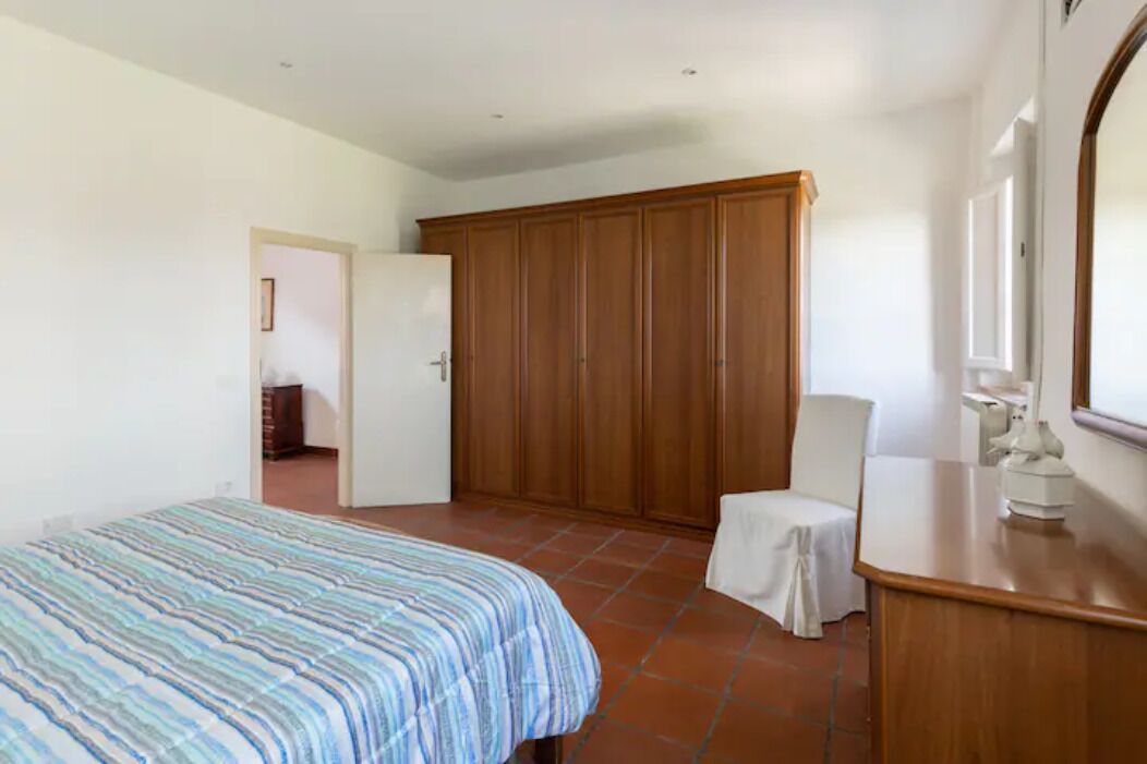 A bedroom with a bed, a wooden wardrobe, a chair, and a nightstand.