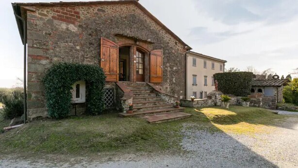 A rustic stone building with wooden shutters, a small staircase leading to a door, and a well-maintained garden area. - Renovated Grange in a Renaissance Villa Park (Capannori)