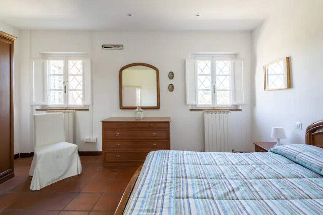 A bedroom with a bed, dresser, chair, and two windows.