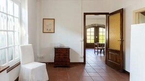 A room with a chair, a dresser, and a door leading to another room. - Renovated Grange in a Renaissance Villa Park (Capannori)