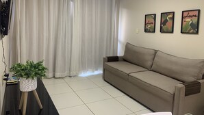 Una sala de estar con un sofá, un televisor montado en la pared y una planta en maceta.