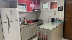 Una cocina equipada con refrigerador, microondas, lavamanos y estufa. Se observan gabinetes, una encimera y una puerta con un letrero.