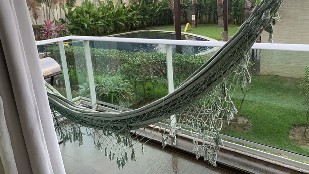 Una hamaca en un balcón con vista a una piscina y abundante vegetación.
