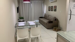 Una sala de estar moderna con una mesa de comedor de vidrio, sillas blancas, un sofá y una lámpara colgante roja.