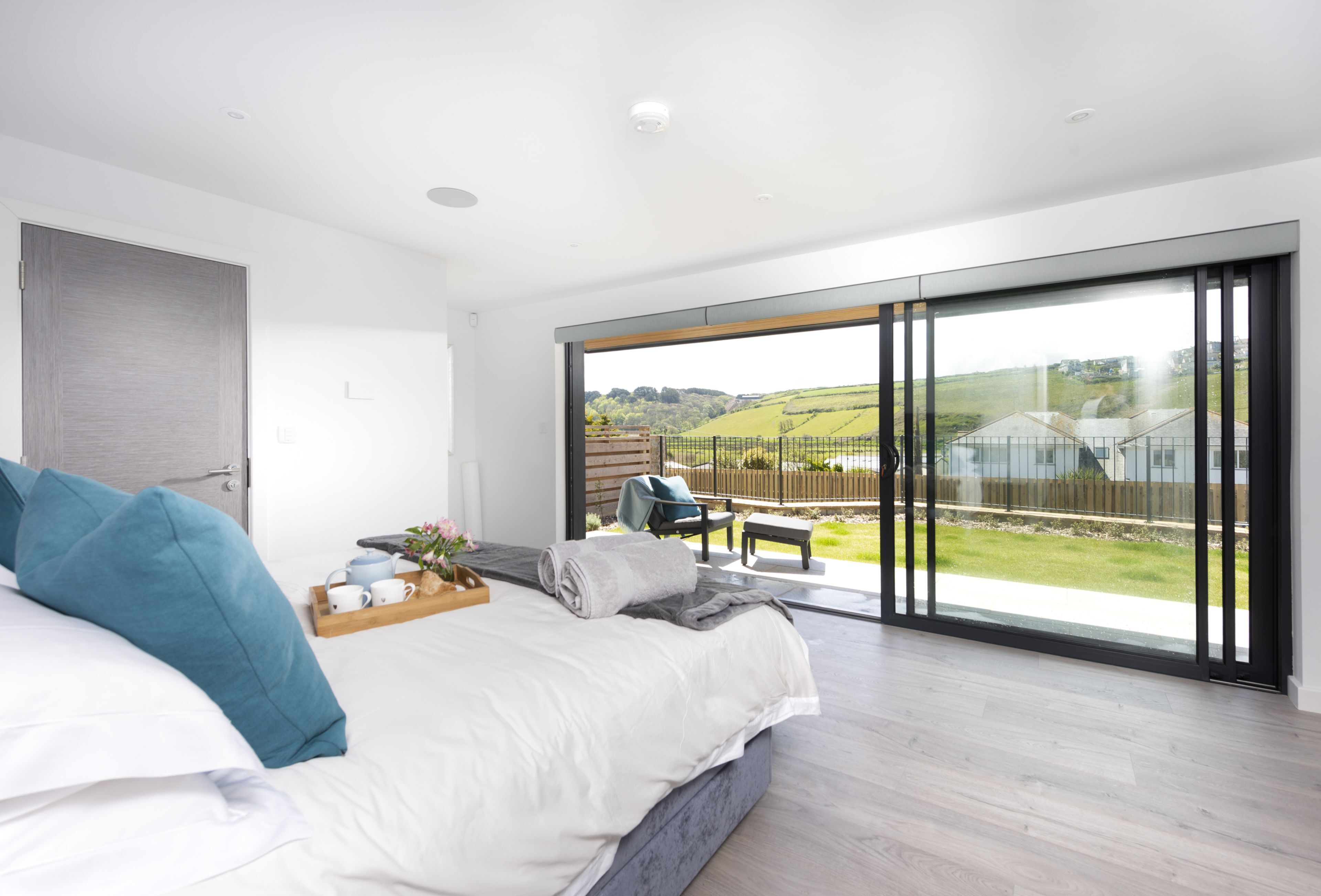 Een slaapkamer met een groot bed, een houten nachtkastje en uitzicht op een tuin door een schuifdeur.