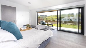 A bedroom with a large bed, a wooden bedside table, and a view of a garden through a sliding glass door. - Stunning and stylish abode, close to the golden sands of Mawgan Porth beach (Mawgan Porth)