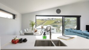 A modern kitchen with a large window, a sink, and a dining area with a view of a rural landscape. - Stunning and stylish abode, close to the golden sands of Mawgan Porth beach (Mawgan Porth)