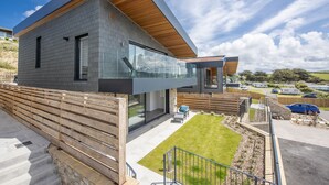 A modern two-story house with a flat roof, large windows, and a wooden deck. - Stunning and stylish abode, close to the golden sands of Mawgan Porth beach (Mawgan Porth)