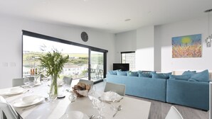 A modern dining area with a large window, a blue sofa, and a painting on the wall. - Stunning and stylish abode, close to the golden sands of Mawgan Porth beach (Mawgan Porth)