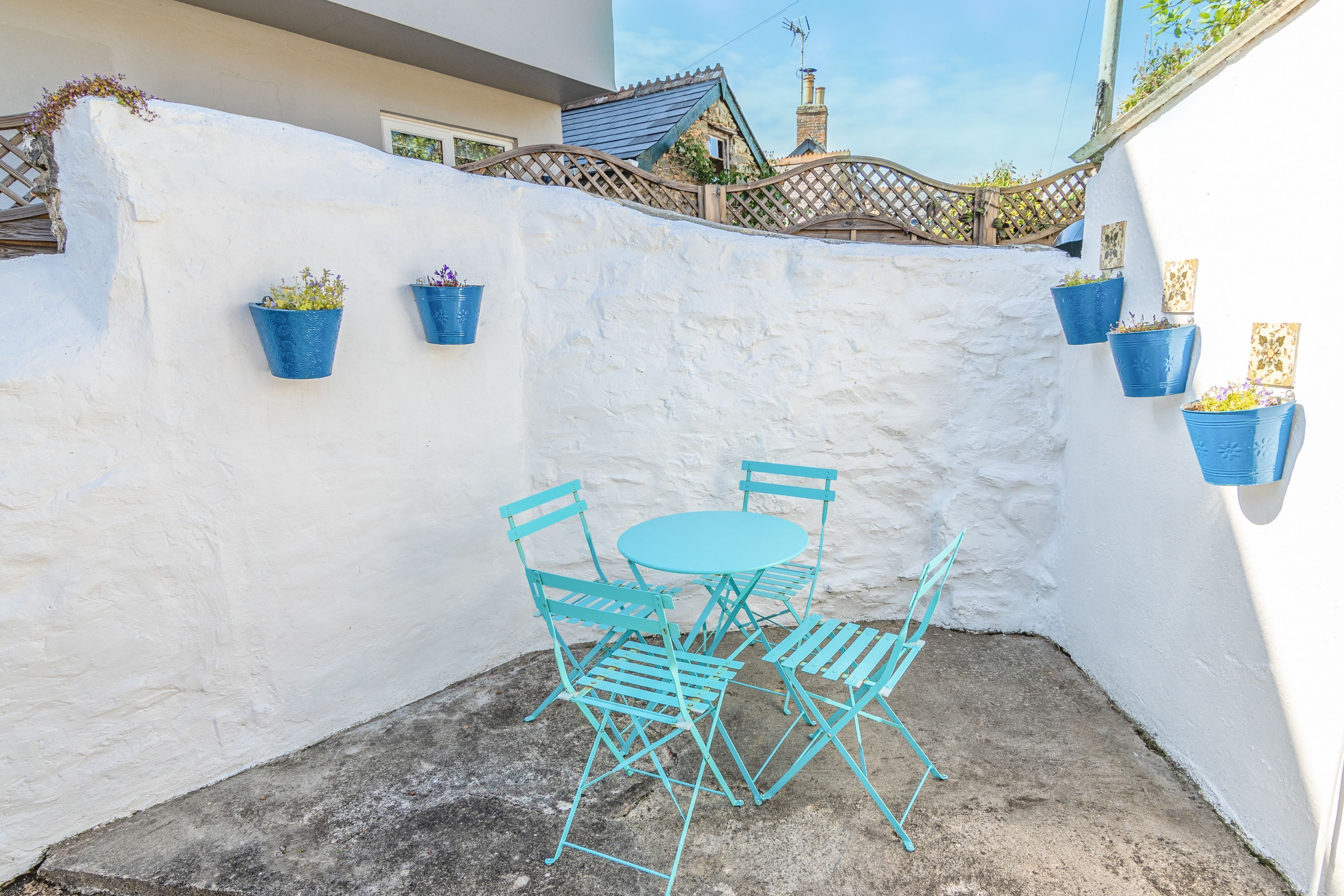 A small outdoor patio with a round table and four chairs, surrounded by white walls and blue planters.