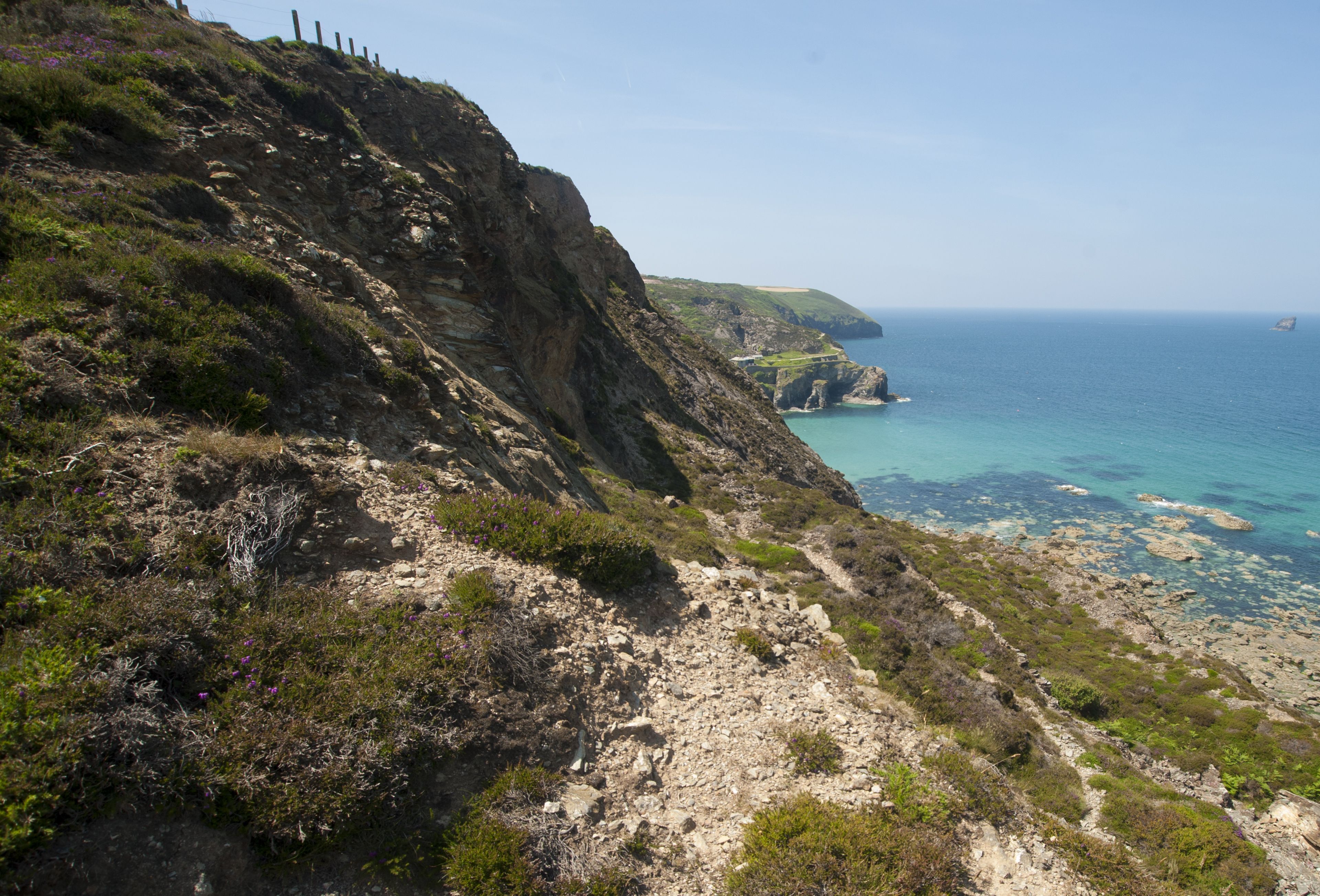 Paesaggio costiero con un sentiero roccioso che conduce a una scogliera con vista sul mare.