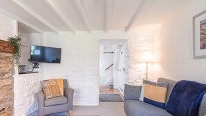 Ein gemütliches Wohnzimmer mit Steinwand, Flachbildfernseher, Sofa, Sessel und Lampe.