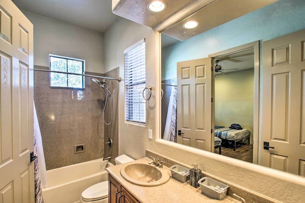 A bathroom with a bathtub, toilet, and sink. There is a window with blinds and a shower area.