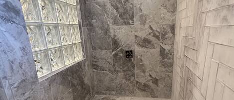 A shower area with marble walls, a herringbone-patterned wall on the right, and a tiled floor.