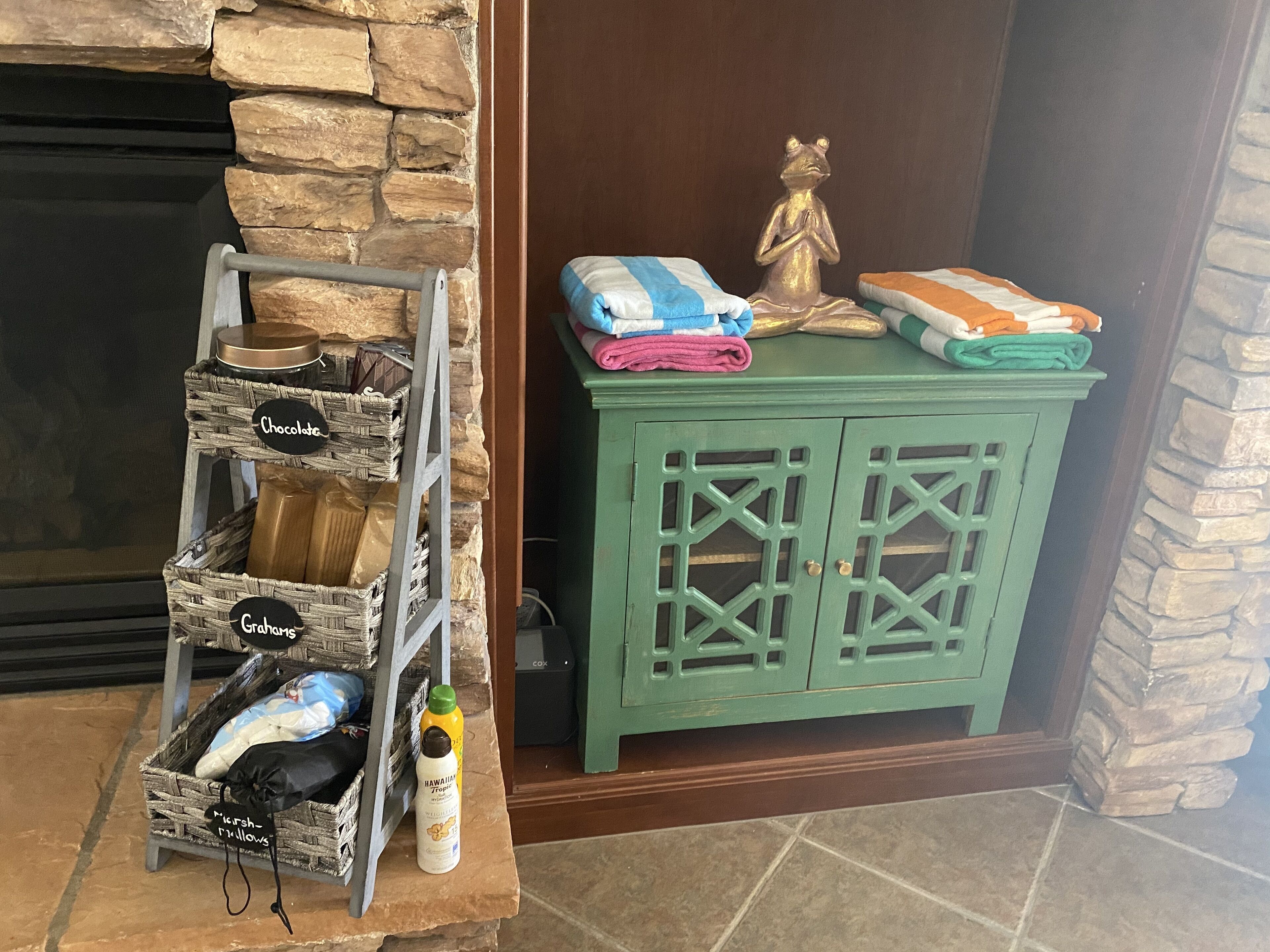 A stone fireplace, a green cabinet with drawers, and a wicker shelf with labeled items.