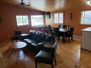 A cozy room with a leather sofa, a dining table with chairs, and a small kitchen area. - Little Tub Harbour Cottage (Northern Bruce Peninsula)