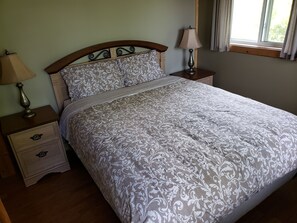 A neatly made bed with a patterned bedspread, two bedside tables with lamps, and a window with curtains. - Little Tub Harbour Cottage (Northern Bruce Peninsula)