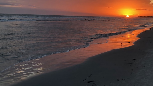 Una playa al atardecer, con el sol poniéndose sobre el océano.