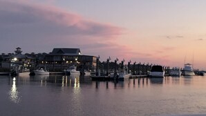 Un puerto deportivo con barcos amarrados, un edificio de varios pisos y una superficie acuática tranquila que refleja el cielo.