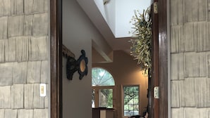 Un vestíbulo amplio con puerta de madera, alfombra estampada y vista a un salón con banco y mesa de comedor.