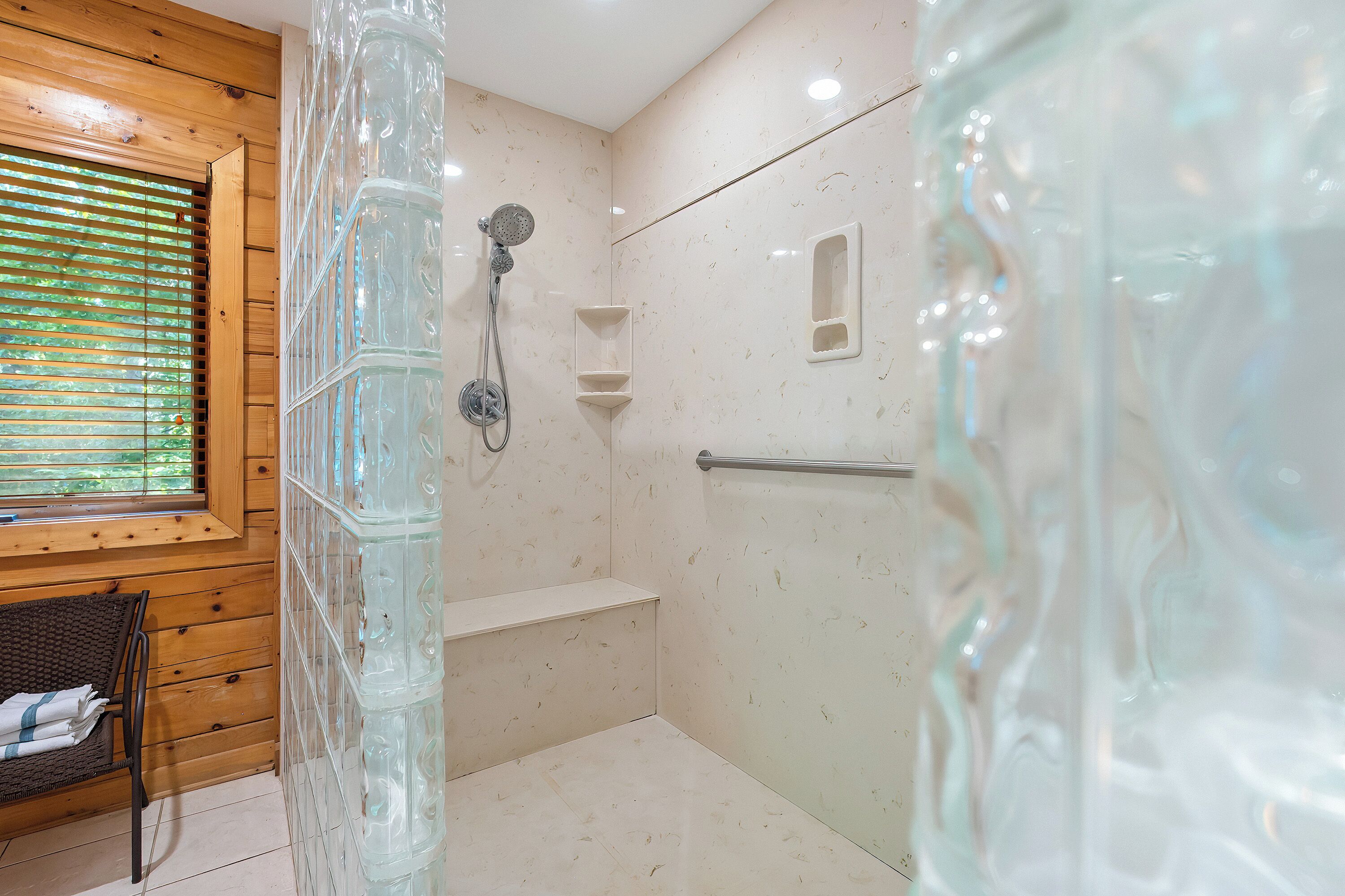 Un baño moderno con cabina de ducha de vidrio, paneles de madera y una ventana con persianas.