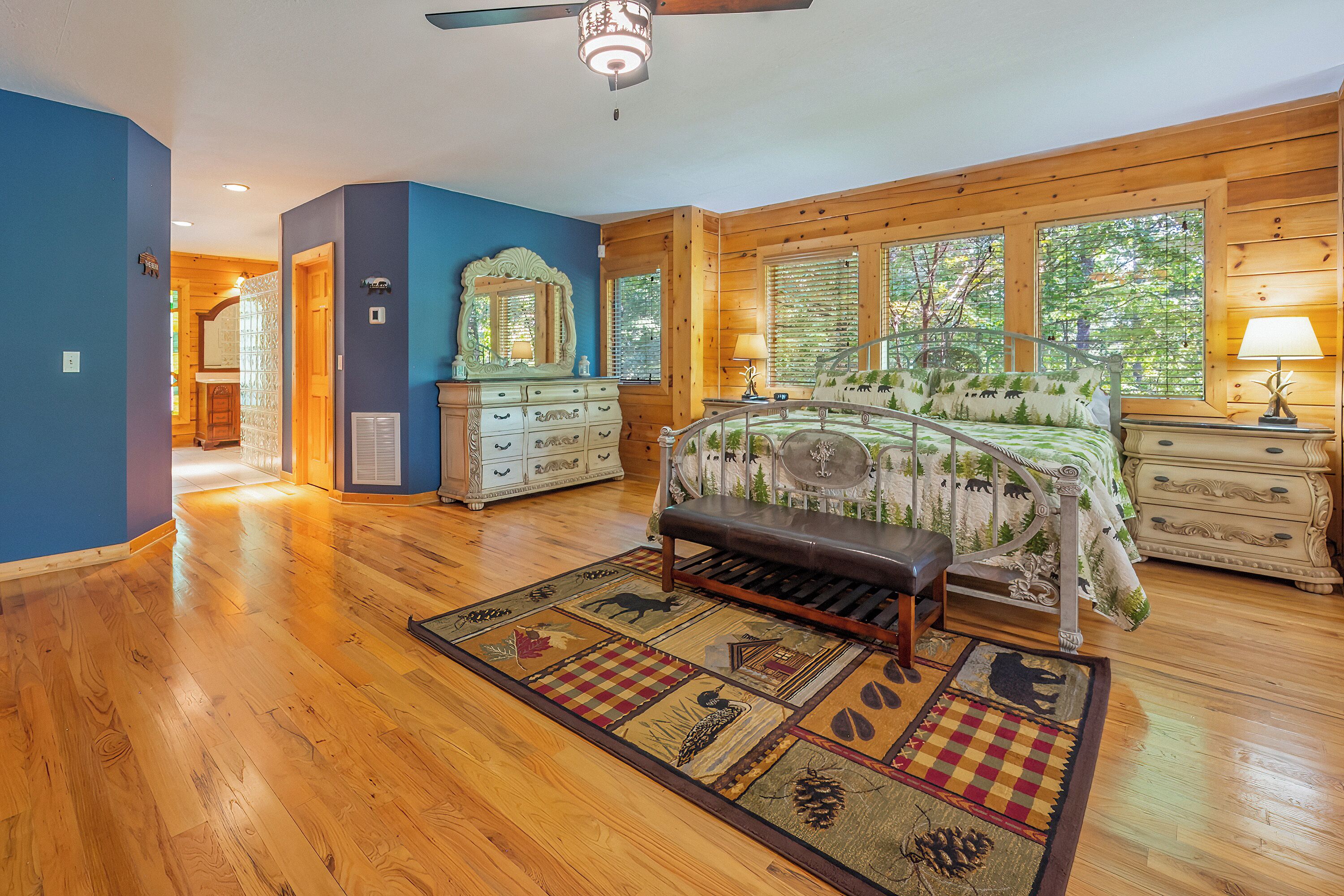A bedroom with a bed, a bench, a dresser, a mirror, and a window with a view of trees.