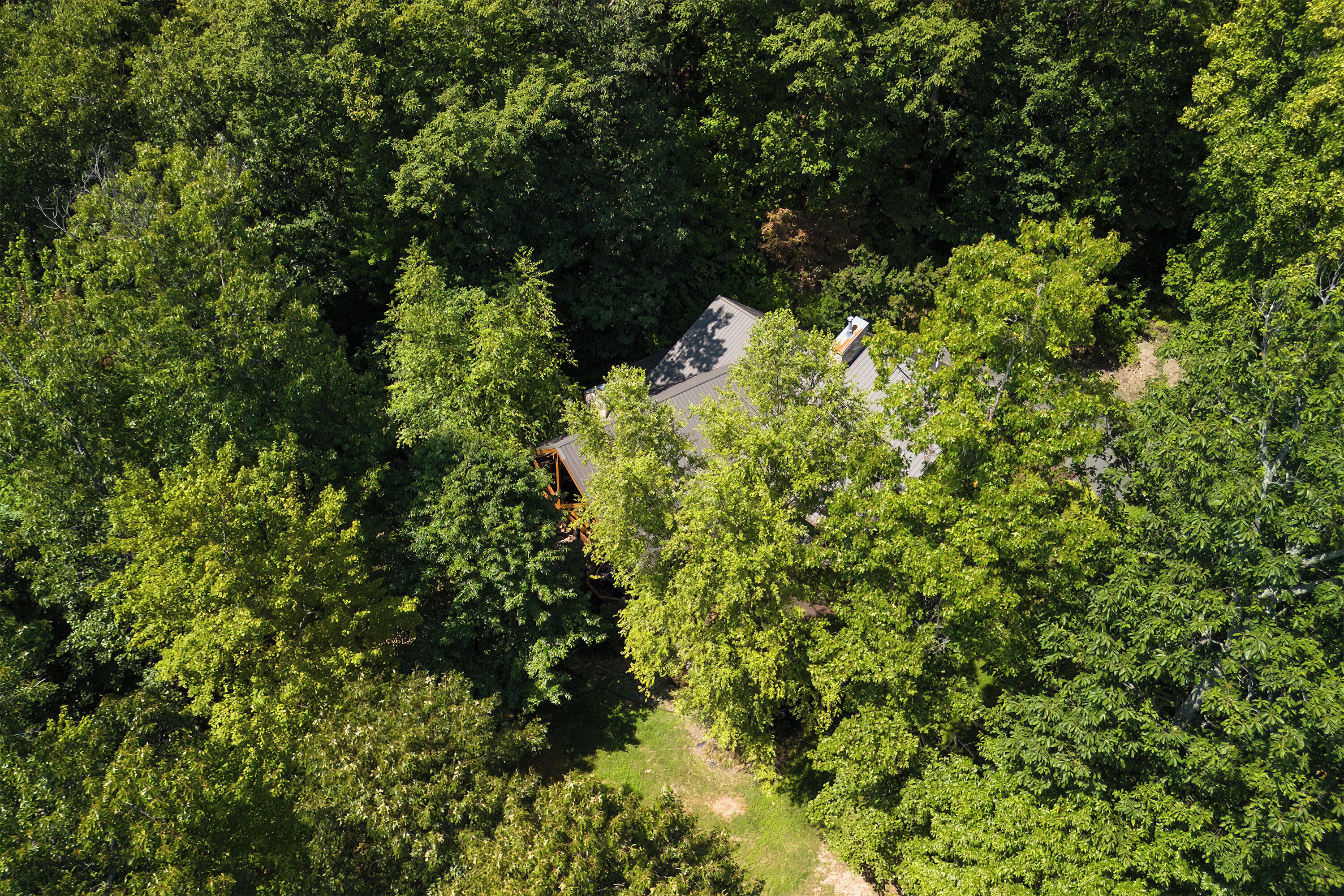 An aerial view of a house surrounded by dense green forest.