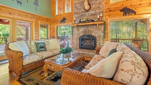 A cozy log cabin interior with wicker furniture, a stone fireplace, and wooden beams. - Now and Forever (Sevierville)