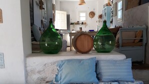 Un soggiorno accogliente con un divano decorato da cuscini a motivi blu e bianchi, un barile di legno e due grandi bottiglie verdi.
