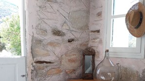 Una stanza rustica con un muro in pietra, un tavolo di legno, uno specchio, un vaso e un cappello appeso al muro.