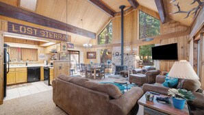 A spacious living area with a large brown sofa, a coffee table, and a TV. There is a kitchen in the background with wooden cabinets and a sign that reads "LOST SIERRA". - Woodsy Mountain Cabin - Best Location In Graeagle (Graeagle)