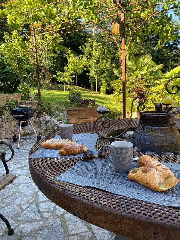 Un área de comedor al aire libre con una mesa redonda de metal, una parrilla y diversos alimentos.