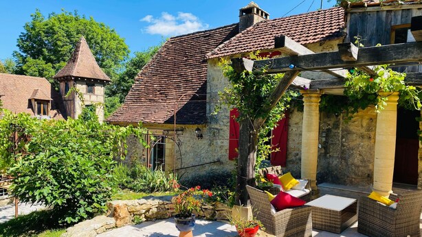 Une cour bordée de murs en pierre, avec une fontaine en pierre et des sièges installés à l’extérieur.