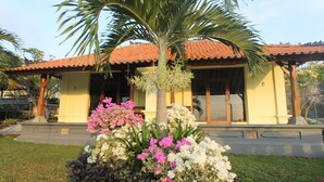 Ein Haus mit Ziegeldach, einer zentralen Palme und einem Blumenbeet mit rosa und weißen Blüten.